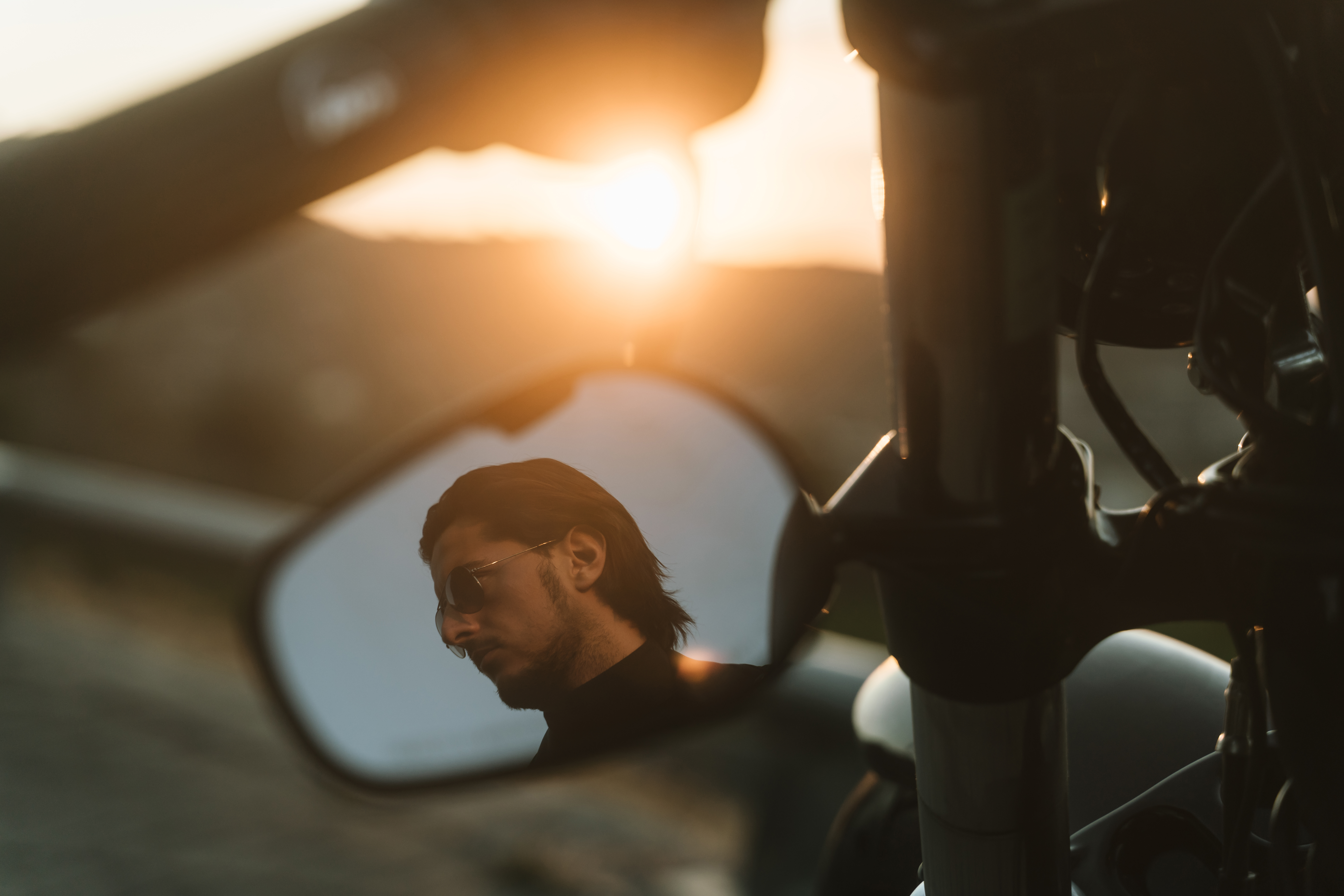 Handsome biker looking away through mirror of his motorcycle